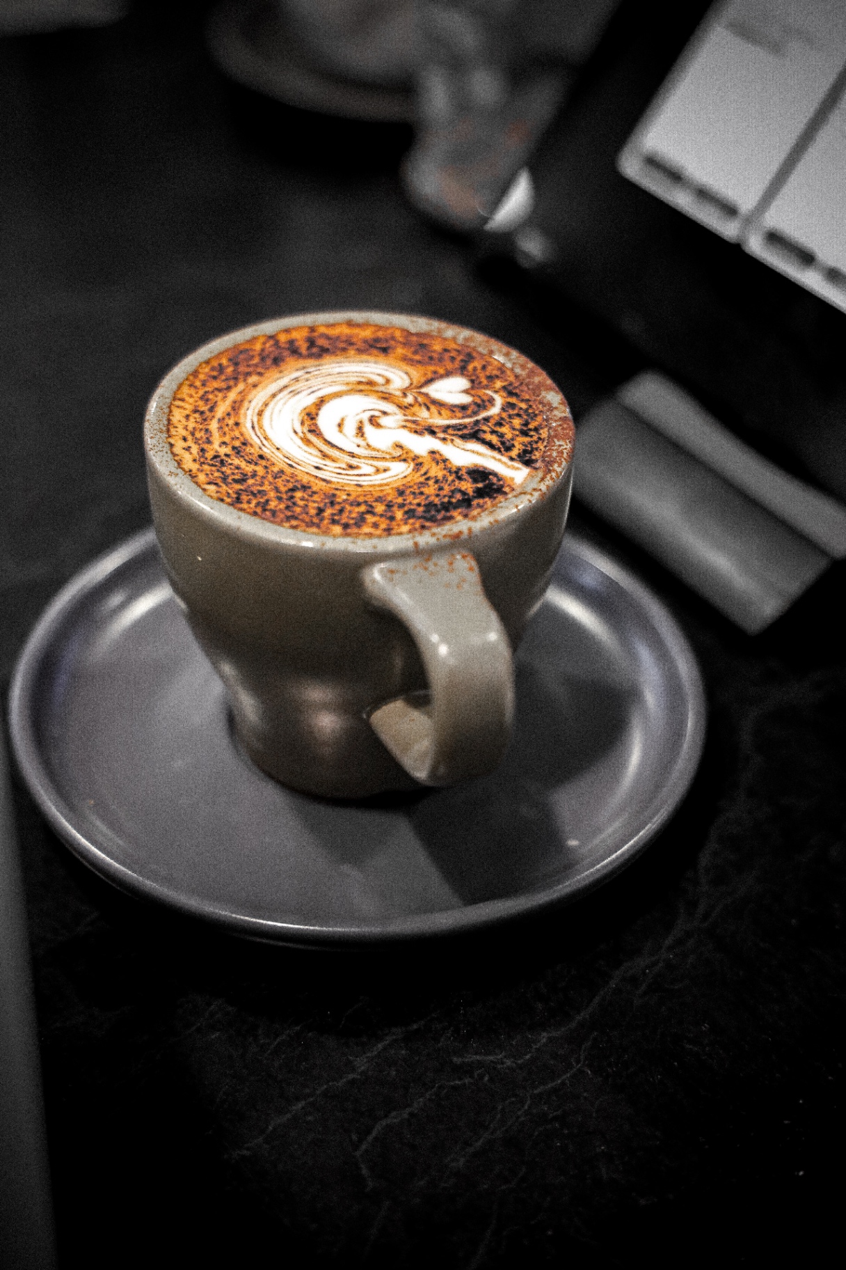 Cappuccino with tulip latte art dusted in cocoa, on dark slate