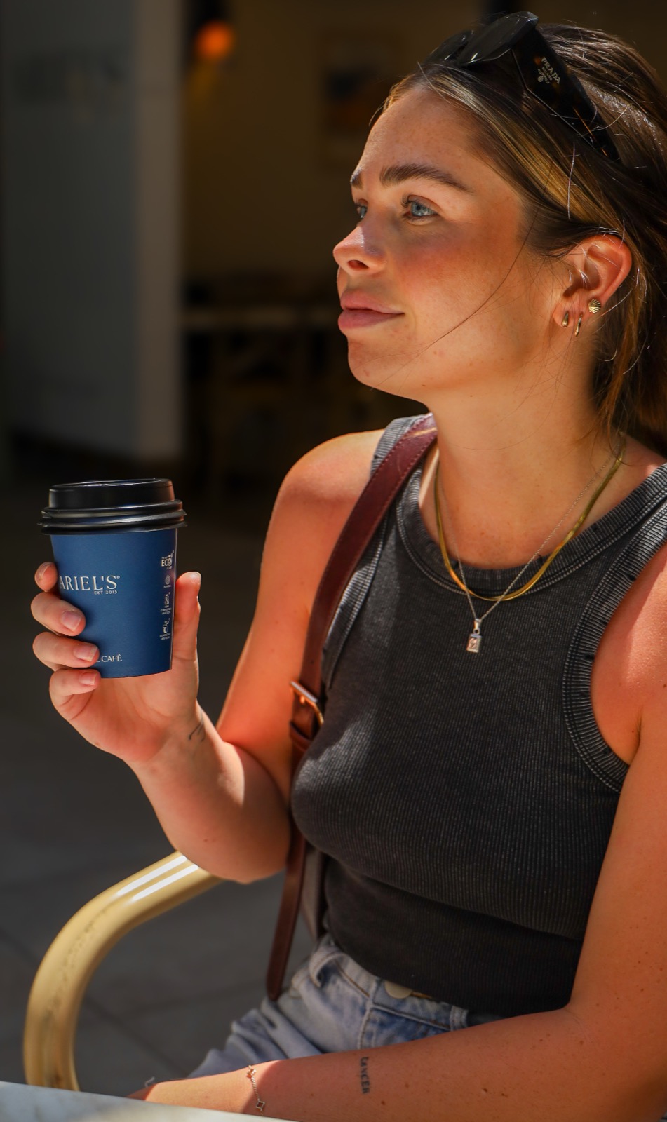 A customer in golden afternoon light holding a navy Ariel's takeaway cup
